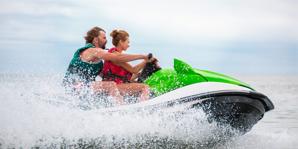 young people having fun driving on high speed on water scooter, man and woman on summer vacation, friends doing active sport